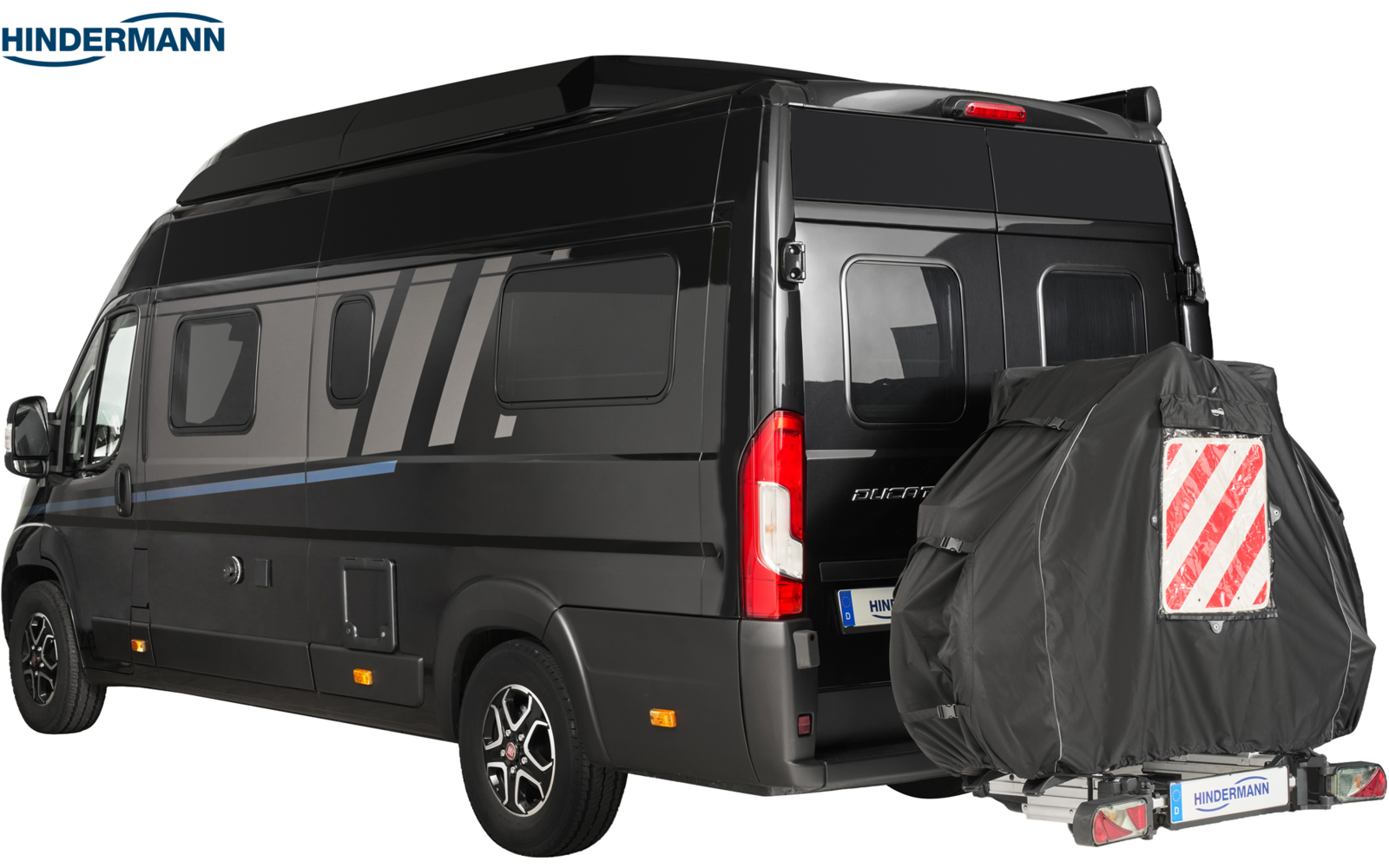 Schwarzer Kastenwagen mit Hochdach und Seitenscheiben, Heckansicht von rechts; montiertes Reserverad mit dunkler Abdeckung und roter-weißer Diagonalwarntafel; Firmenlogo "HINDERMANN" oben links
