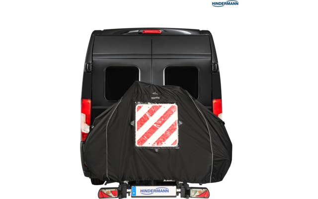 Heckansicht eines schwarzen Transporters mit zwei rechteckigen Heckfenstern; an der Rückseite ein schwarzer Überzug mit einem weißen Schild und roten diagonalen Streifen; Rücklichter und Kennzeichen 'HINDERMANN' sichtbar