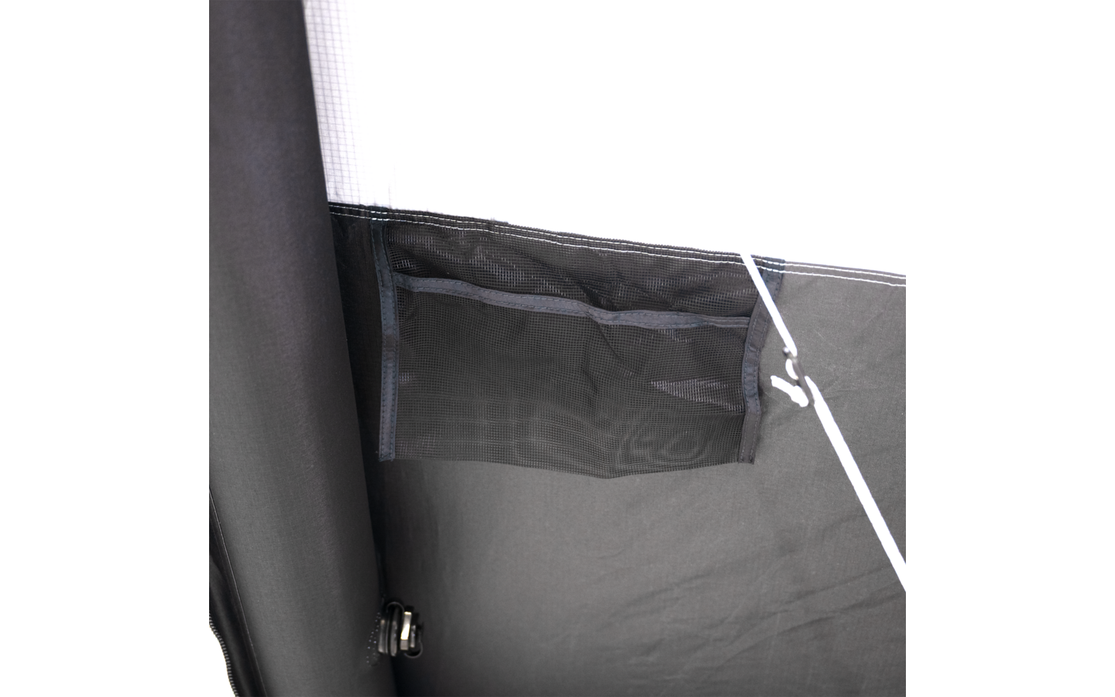 Dunkler Stoff mit eingenähtem rechteckigem Netzfach, weiße Schnur verläuft diagonal, links ein schwarzer Rohrpfosten mit Metallbefestigung