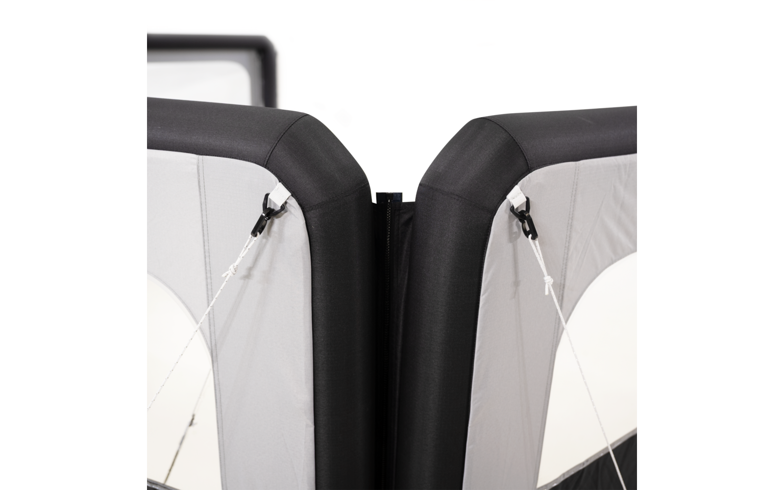 Zwei nebeneinander stehende Polster mit schwarzem Rand und grauen Stoffflächen, in der Mitte ein schmaler Spalt; an den Seiten weiße Spannseile mit schwarzen Clips