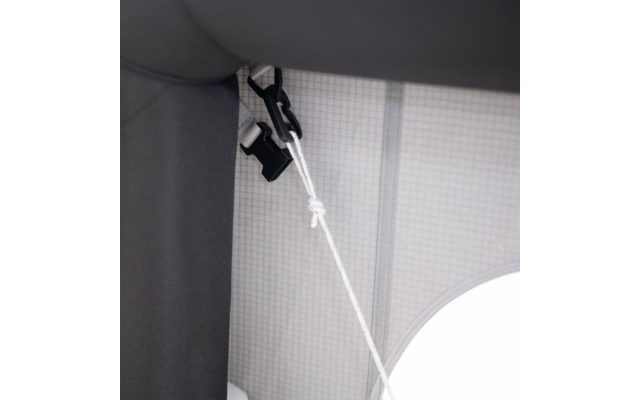 Schwarze Kunststoffklemme an grauer Polsterfläche, daran ein verknotetes weißes Seil; Hintergrund: gitterförmiger Sichtschutz und teilweiser runder weißer Lampenschirm