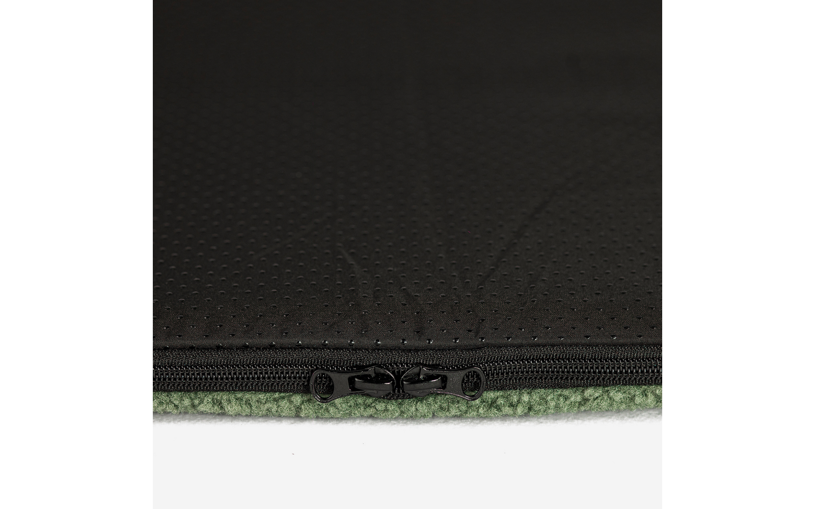 Nahaufnahme eines schwarzen Reißverschlusses an perforiertem schwarzem Stoff über grünem Fleece vor weißem Hintergrund