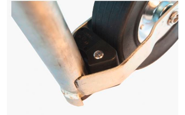 Zwart rubberwiel op een metalen beugel met zichtbare schroef naast een metalen buis