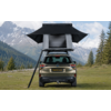 Rear view of an SUV on a grassy meadow with an open rooftop tent and ladder, conifer trees and snow-capped mountains under a cloudy sky