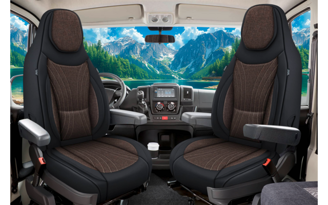 Innenraum eines Fahrzeugs mit zwei braunen drehbaren Vordersitzen und Armlehnen, Lenkrad und Armaturenbrett; durch die Windschutzscheibe sichtbarer Bergsee mit Bergen, Wald und blauem Himmel