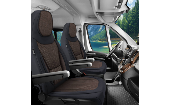 Innenraum eines Fahrzeugs mit zwei braunen Polstersitzen mit Armlehnen, Lenkrad und Armaturenbrett; durch die Scheibe sichtbar ein See, Wald und Berge