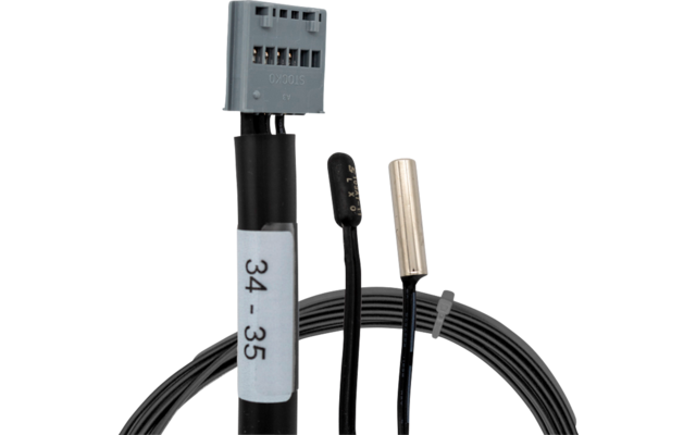 Nahaufnahme von Kabeln: grauer Mehrfachstecker, schwarzes Kabel mit blauem Etikett "34 - 35", zwei kleine zylindrische Bauteile (eins schwarz mit goldenen Punkten, eins silbermetallic), Kabelbündel mit Kabelbinder vor weißem Hintergrund