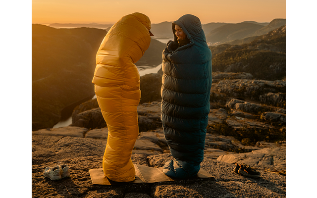 Twee personen staan op een rotsplateau bij zonsondergang, elk in een slaapzakachtig pak (geel, donkerblauw) op matjes; schoenen naast hen; water en bergen op de achtergrond