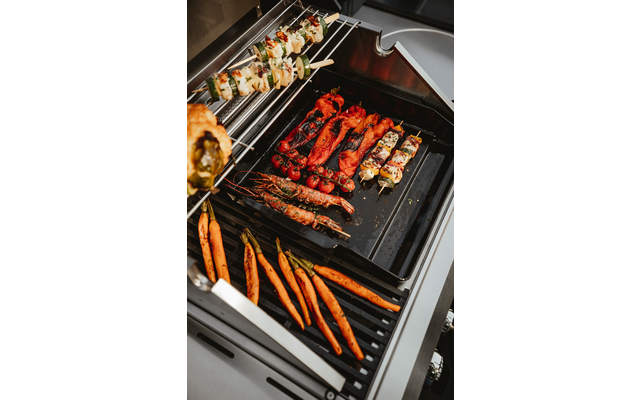 Gasbarbecue met verschillende spiesjes en groenten: hele wortels, garnalen met schaal, spiesjes met vlees- en groentestukken
