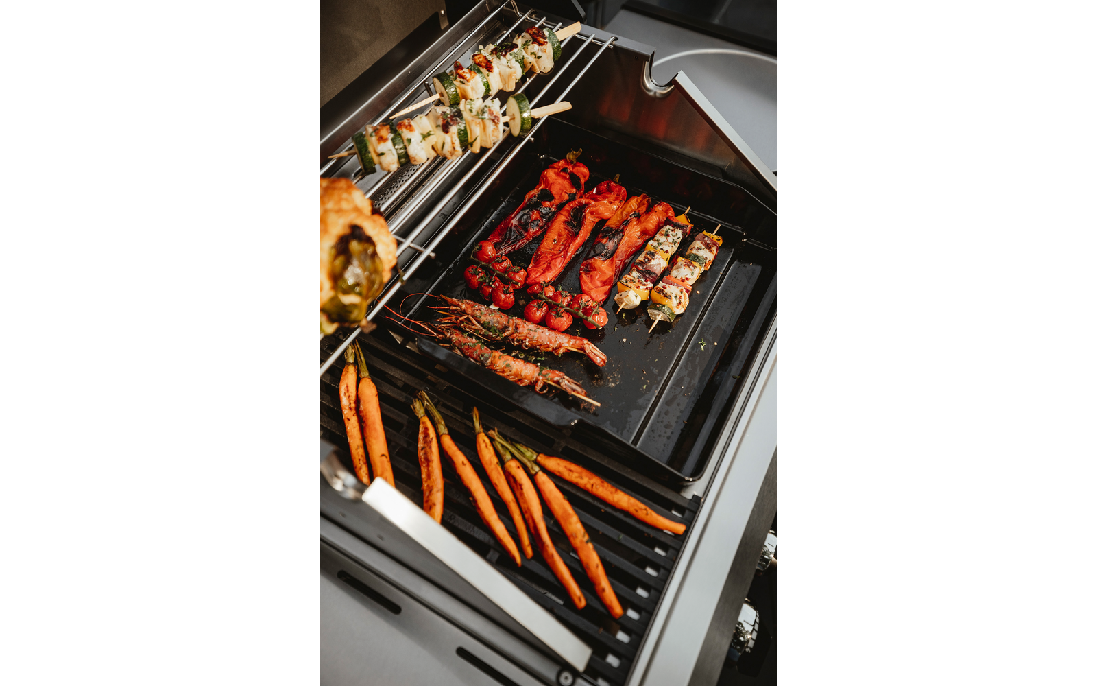 Gasbarbecue met verschillende spiesjes en groenten: hele wortels, garnalen met schaal, spiesjes met vlees- en groentestukken