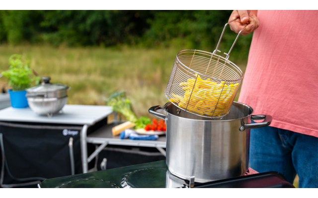 Person gießt Nudeln aus einem Topf in ein Sieb im Freien
