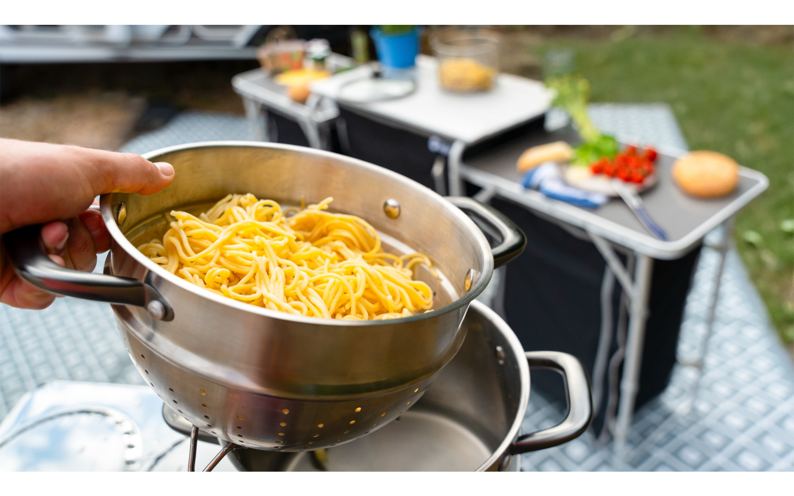 Hand hält eine Schüssel mit geriebenem Käse über einem Campingkocher