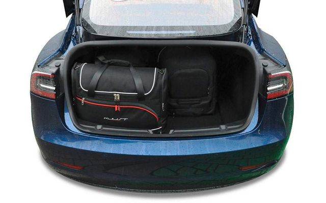 Coffre ouvert d'une voiture bleue avec à gauche un sac de voyage noir avec des accents rouges et à droite un sac à dos noir
