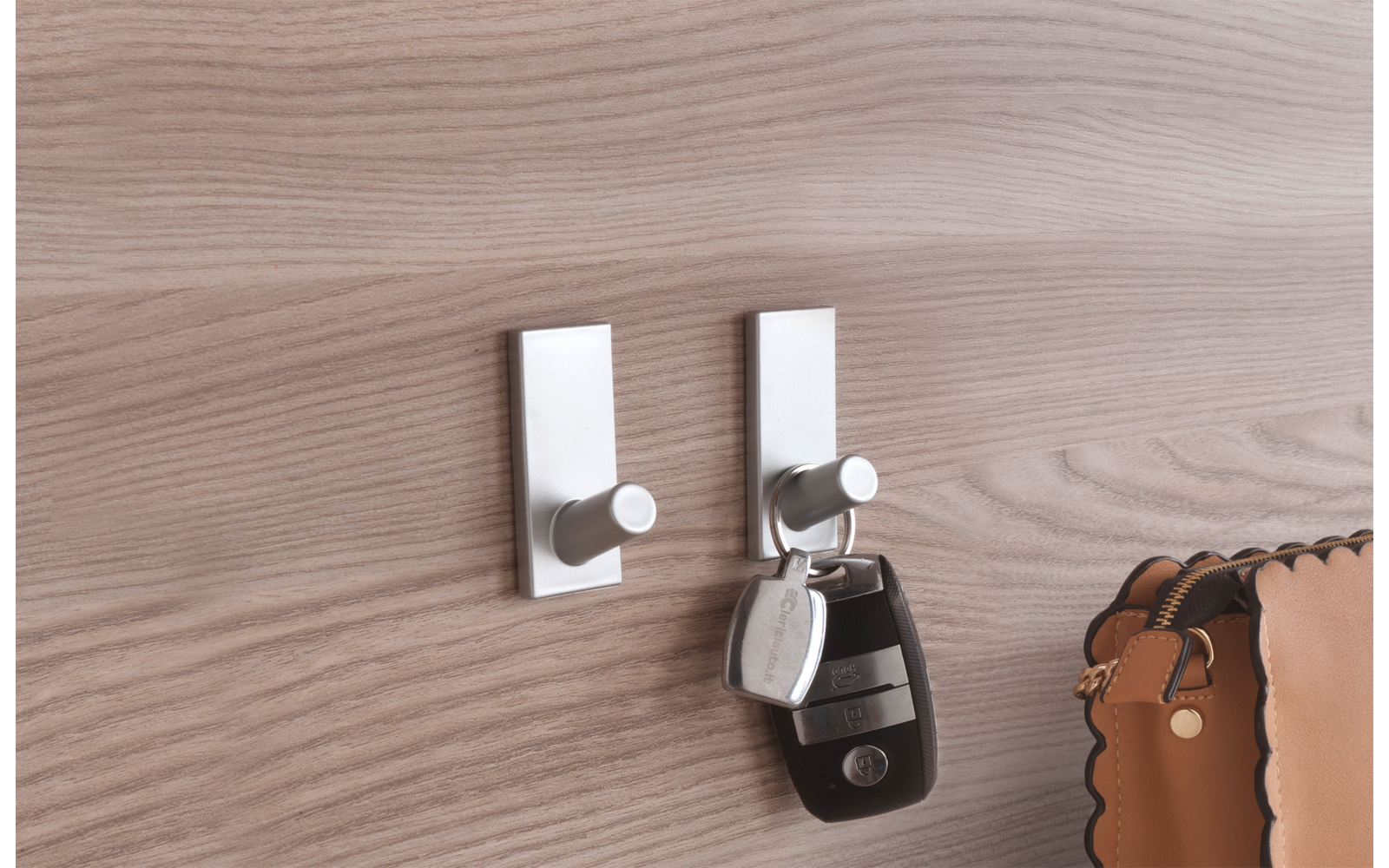 Zwei weiße Wandhaken mit einem schwarzen Schlüsselbund und einem braunen Taschenanhänger