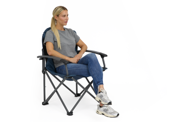 Person sitzt in klappbarem Campingstuhl mit übereinander geschlagenen Beinen, trägt graues T‑Shirt, blaue Jeans und weiße Sneakers, blickt nach rechts