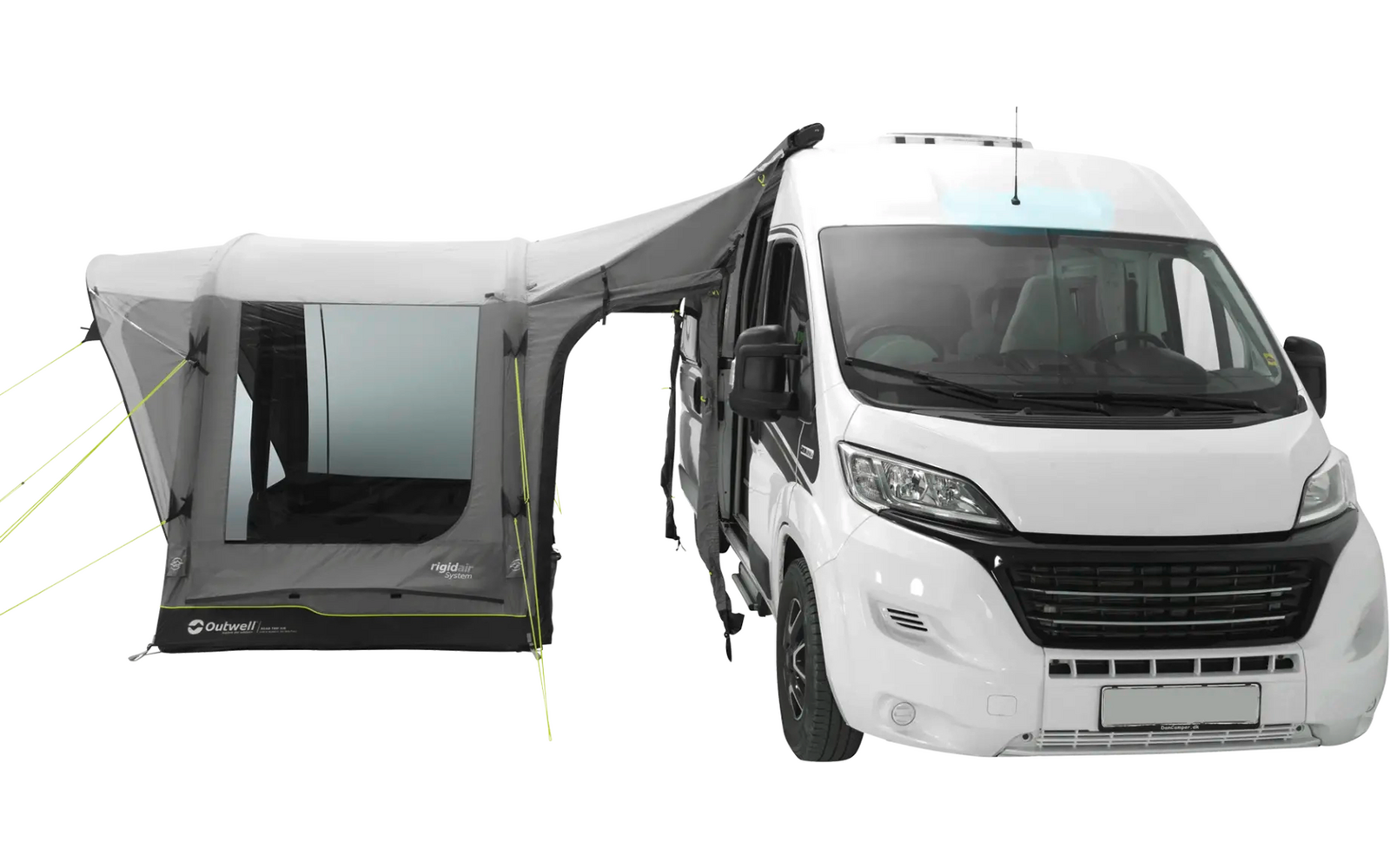 Camper bianco, parte anteriore e lato destro visibili; a sinistra una tenda/auvent grigia collegata con ampie finestre, pali e tiranti visibili