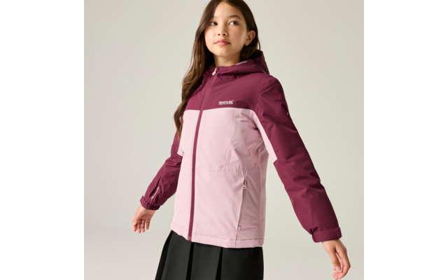 Fille aux cheveux foncés jusqu'aux épaules, porte une veste à capuche bicolore (haut magenta foncé, bas rose clair) avec fermeture éclair et poches latérales, jupe noire, debout devant un fond uni clair et regardant sur le côté
