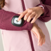 Gros plan de mains appuyant sur un module lumineux blanc dans un boîtier noir sur la manche d'une veste rose clair et bordeaux; fermeture éclair et velcro visibles