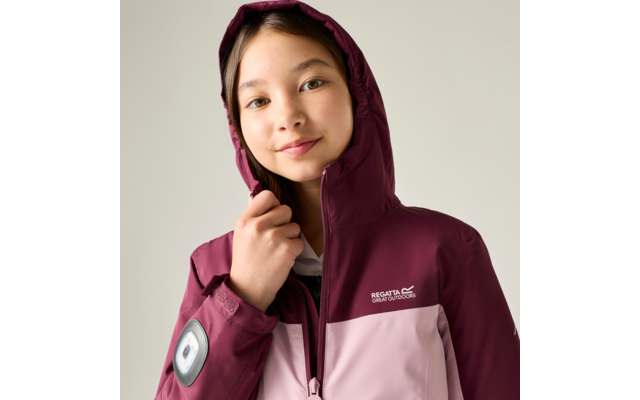 Fille portant une veste à capuche bordeaux et rose clair, capuche portée, tenant la fermeture éclair, logo de marque visible sur la poitrine, écusson rond sur la manche gauche