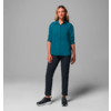 Femme debout devant un fond gris, porte une chemise bleue et un pantalon noir