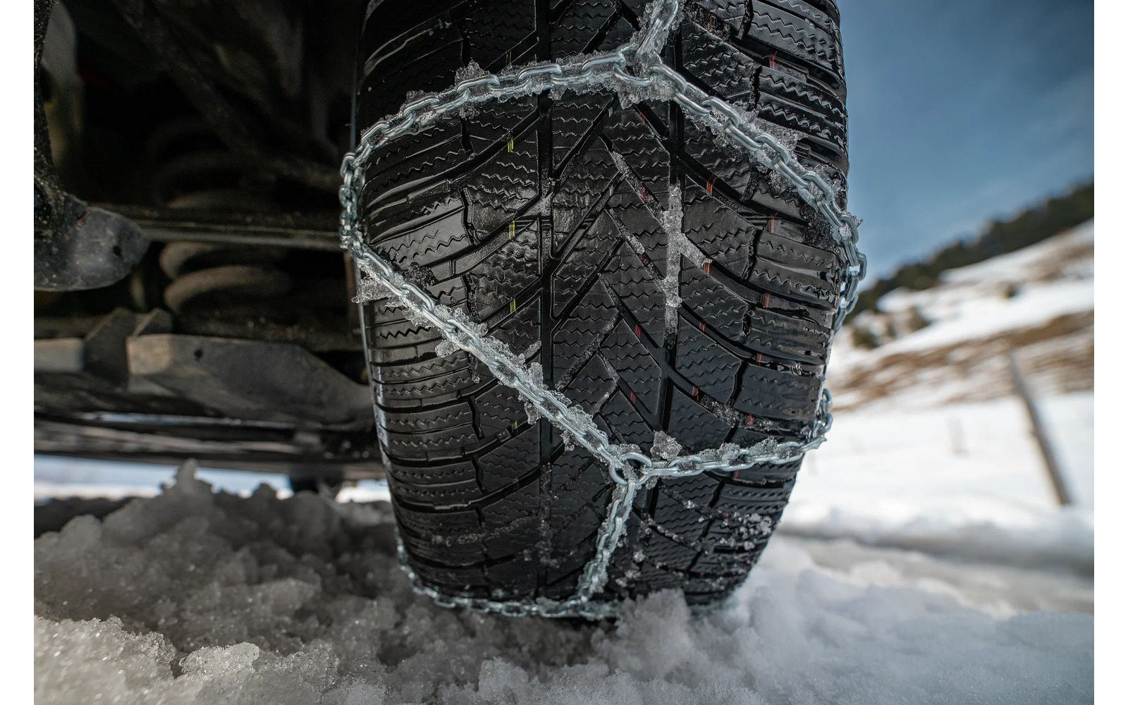 Primer plano de un neumático de coche con cadenas para nieve en una carretera nevada