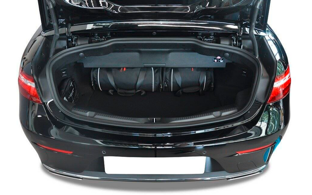 Coffre arrière noir ouvert d'une voiture avec trois sacs de voyage noirs à l'intérieur, feux arrière visibles et emplacement de plaque d'immatriculation blanc
