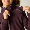 Close-up des unteren Gesichts und Oberkörpers einer Person mit geschlossenen Lippen; dunkelviolette Reißverschlussjacke, Hände halten Kragen und Schulter; kleines Logo auf der Schulter