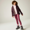 Kind mit lockigem Haar steht leicht geneigt, trägt eine dunkelviolette Jacke, einen hellrosa Kapuzenpullover, pinke Leggings mit Blumenmuster und graue Wanderschuhe mit rosafarbenen Details vor hellem Hintergrund