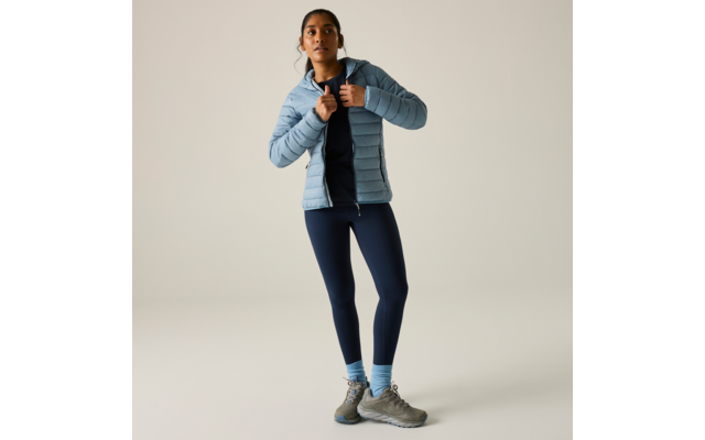 Person steht, trägt hellblaue gesteppte Jacke, dunkles Oberteil, dunkelblaue Leggings, hellblaue Socken und graue Wanderschuhe, Hände am Kragen der Jacke