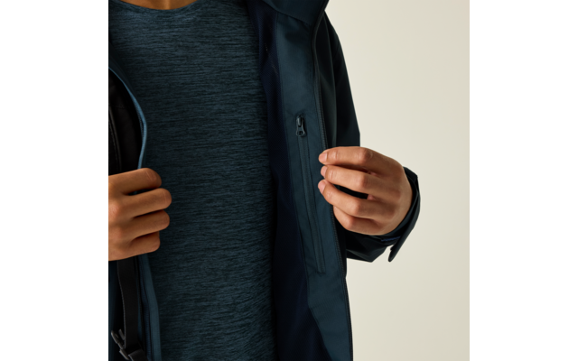 Person öffnet eine dunkelblaue Jacke mit einer Hand; sichtbar sind ein dunkelblaues meliertes T‑Shirt und eine Innentasche mit Reißverschluss