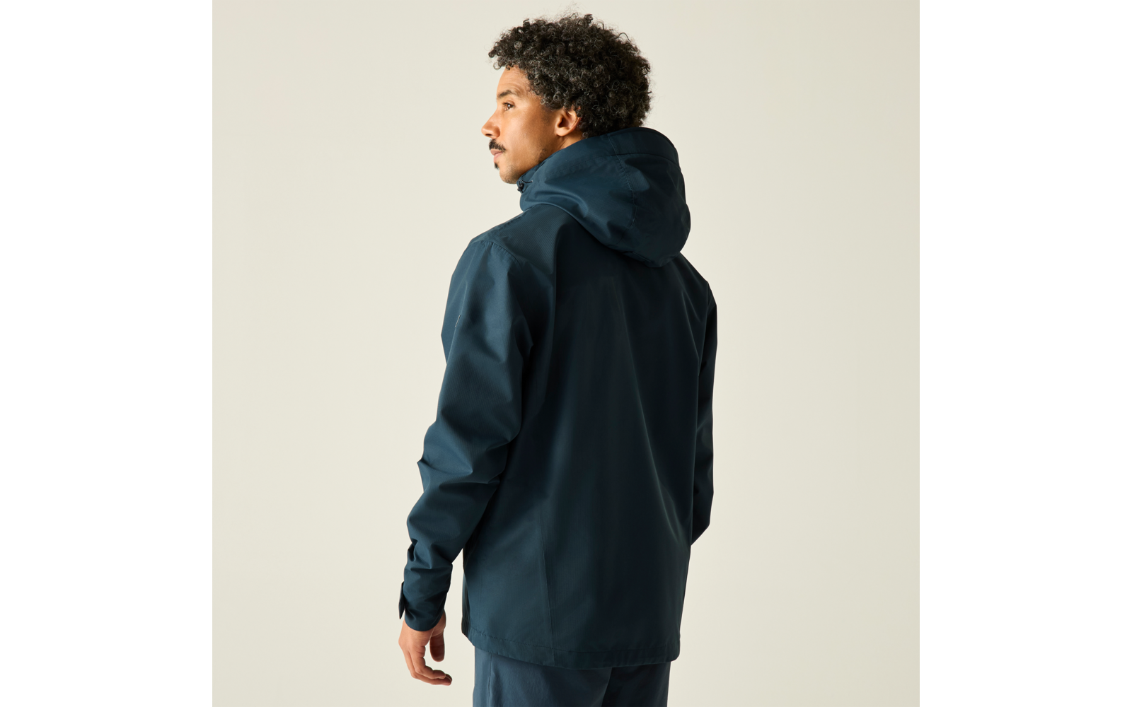 Person in dunkelblauer Kapuzenjacke, halb von hinten, schaut nach links vor hellem Hintergrund