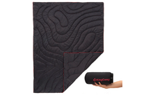 Schwarzer, zusammengefalteter Schlafsack mit roten Nähten, gehalten von einer Hand neben einer zusammengerollten Tragetasche