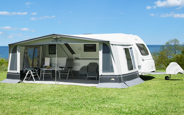 Caravana con toldo sobre césped verde bajo un cielo azul