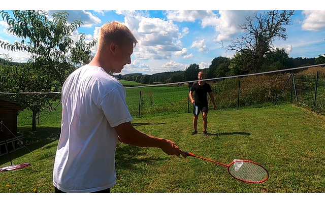 Zwei Jungen spielen Badminton auf einem grasbewachsenen Feld unter blauem Himmel mit Wolken