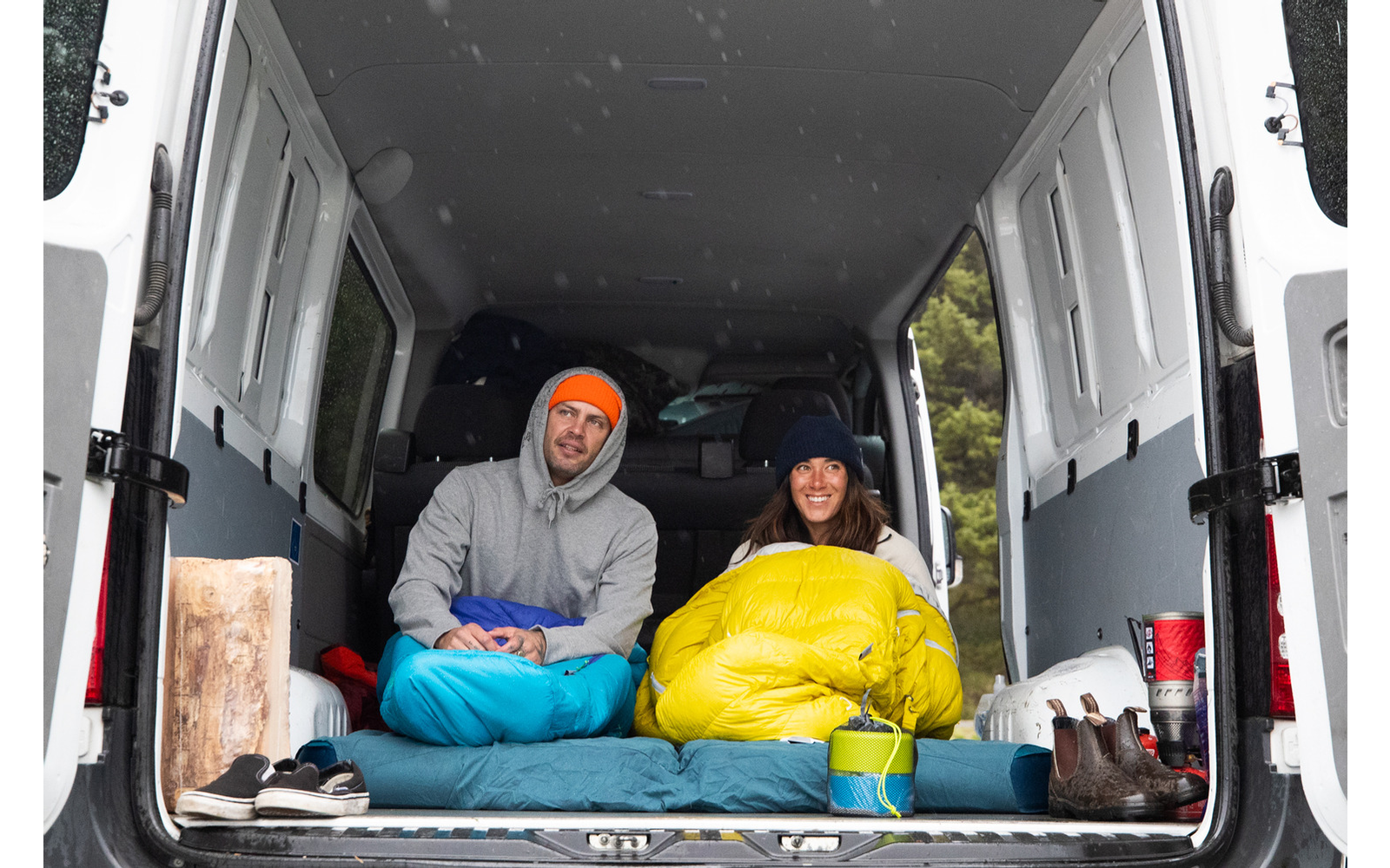 Zwei Personen sitzen in einem Lieferwagen, eine trägt orange, die andere gelbe Kleidung