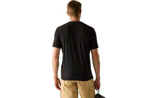 Rückansicht einer Person mit kurzem Haar, schwarzem T‑Shirt, beigen Cargo-Shorts und einer dunklen Kappe in der rechten Hand vor hellem Hintergrund