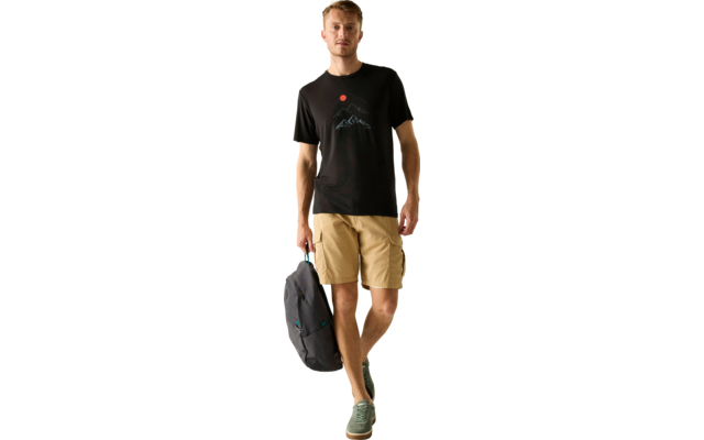 Ein Mann geht, trägt ein schwarzes T‑Shirt mit Berg- und roter Sonnen‑Grafik, beige Cargo‑Shorts, grüne Sneaker und hält einen grauen Rucksack in einer Hand vor hellem Hintergrund