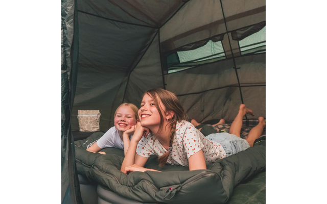 Zwei Mädchen liegen lächelnd auf Schlafsäcken in einem Zelt