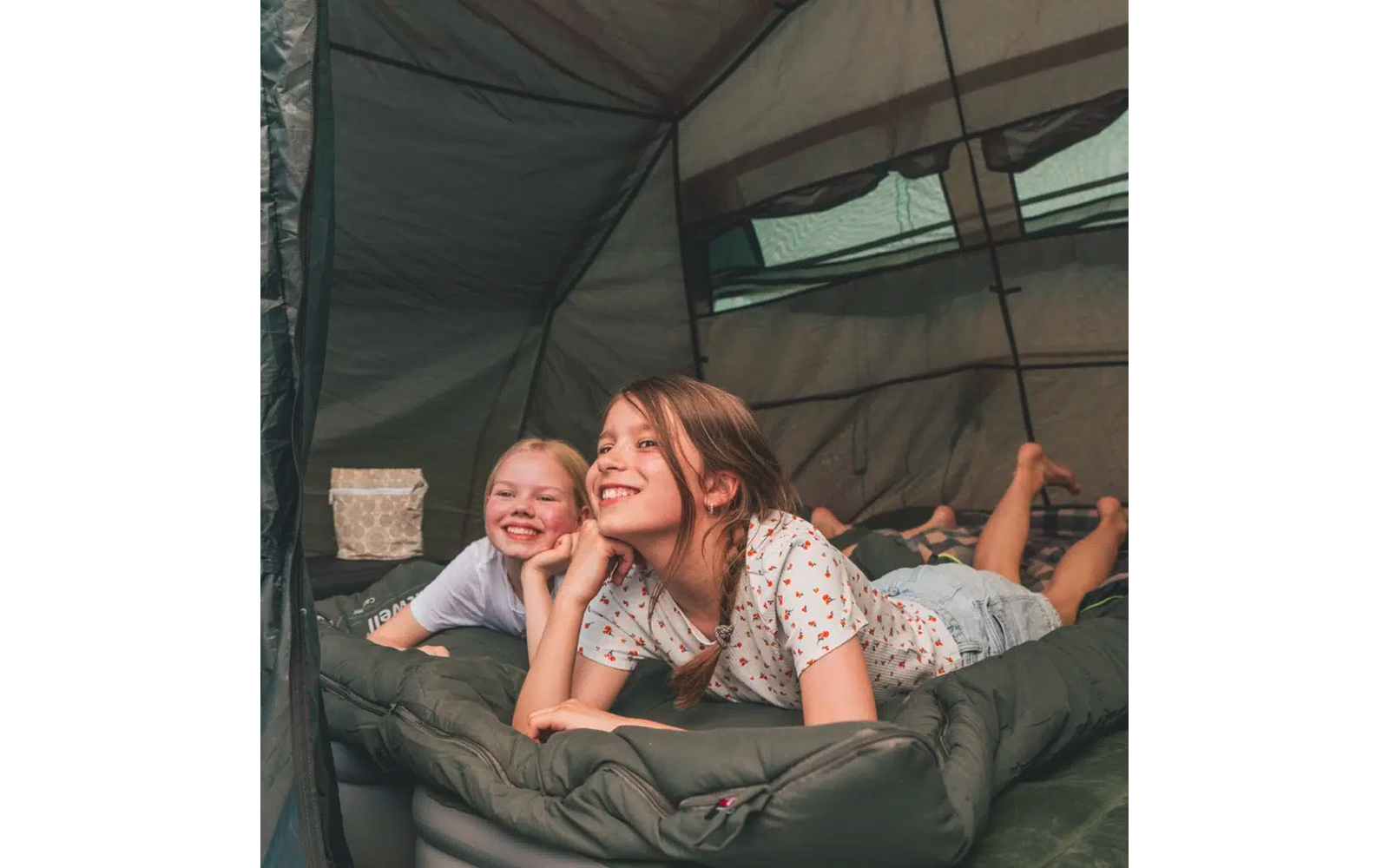 Zwei Mädchen liegen lächelnd auf Schlafsäcken in einem Zelt