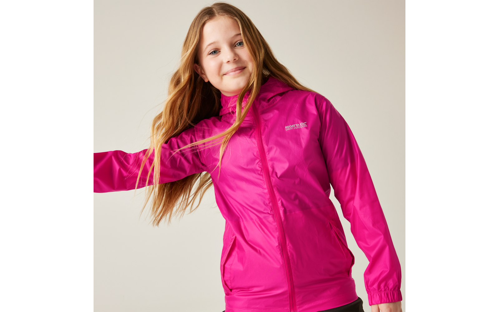 Person with long blonde hair wearing a pink hooded jacket, one arm extended, light background