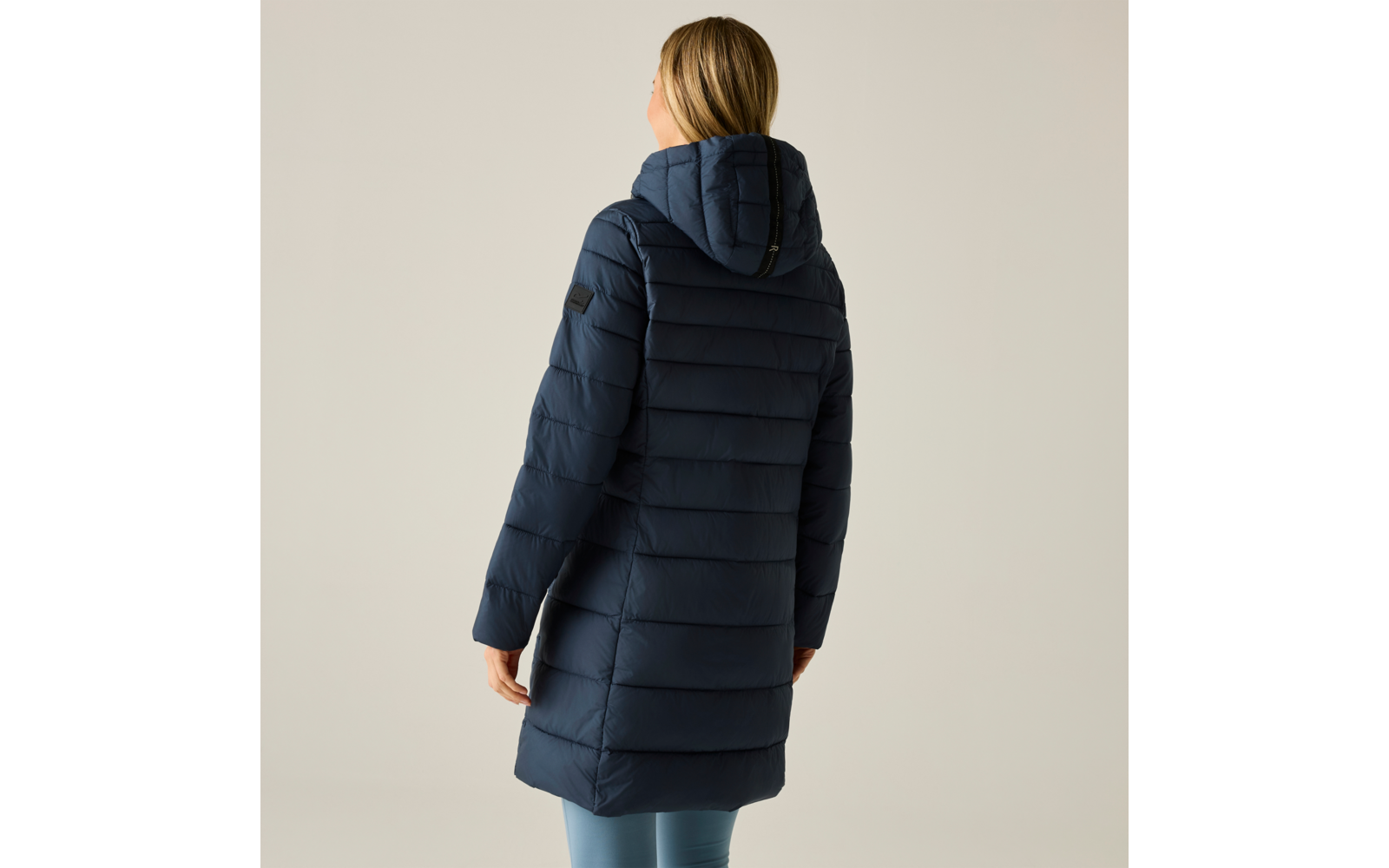 Persona vista di spalle, indossa un piumino trapuntato con cappuccio blu scuro e leggings azzurri, sfondo chiaro uniforme