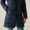 Parte centrale del corpo di una persona con un giaccone imbottito blu scuro sopra leggings azzurri, mano sinistra in tasca, mano destra visibile, cerniera inferiore aperta, sfondo chiaro