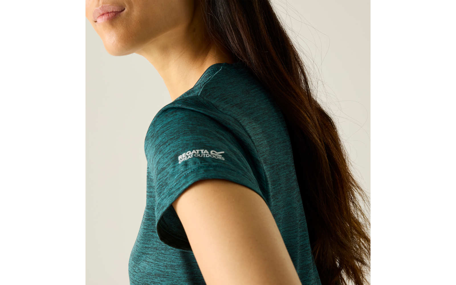 Close-up van een persoon van schouder tot kin, lang donker haar, turquoise T-shirt met korte mouwen en wit logo op de mouw