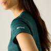 Close-up van een persoon van schouder tot kin, lang donker haar, turquoise T-shirt met korte mouwen en wit logo op de mouw
