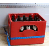 Red plastic crate with 16 empty beer bottles on a wooden floor