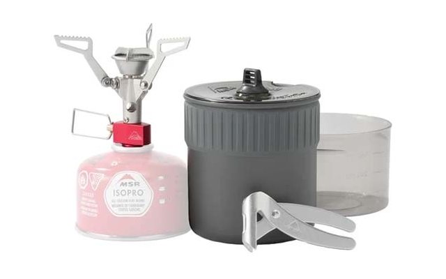 Cartucho de gas de camping rosa con la inscripción "MSR ISOPRO" y un quemador plateado acoplado; junto a él una olla gris con tapa y asa metálica plegable y un recipiente de plástico transparente