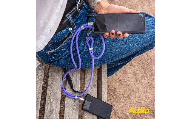 Hand hält ein Smartphone, verbunden über ein violettes Ladekabel mit einer schwarzen Powerbank auf einer Holzbank; Person trägt blaue Jeans und eine Armbanduhr; gelbes "Aqila"-Logo unten rechts