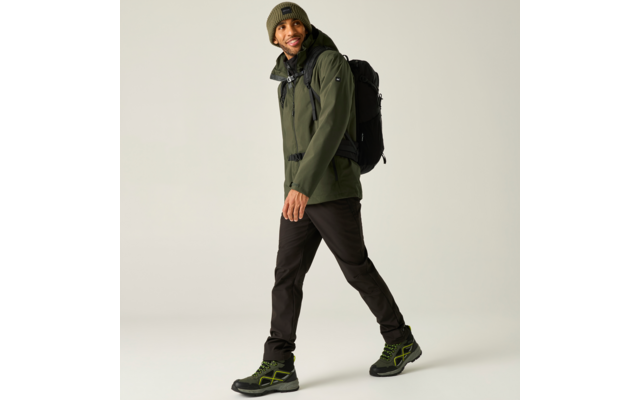 Persoon loopt, draagt een groen jack, een groene gebreide muts, een zwarte rugzak, zwarte broek en zwarte schoenen met groene details op een lichte achtergrond