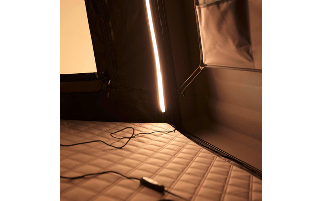 Gesteppte Matte auf dem Boden, schwarzes Stromkabel mit Inline-Schalter darauf, vertikale LED-Lichtleiste an dunkler Stoffinnenwand