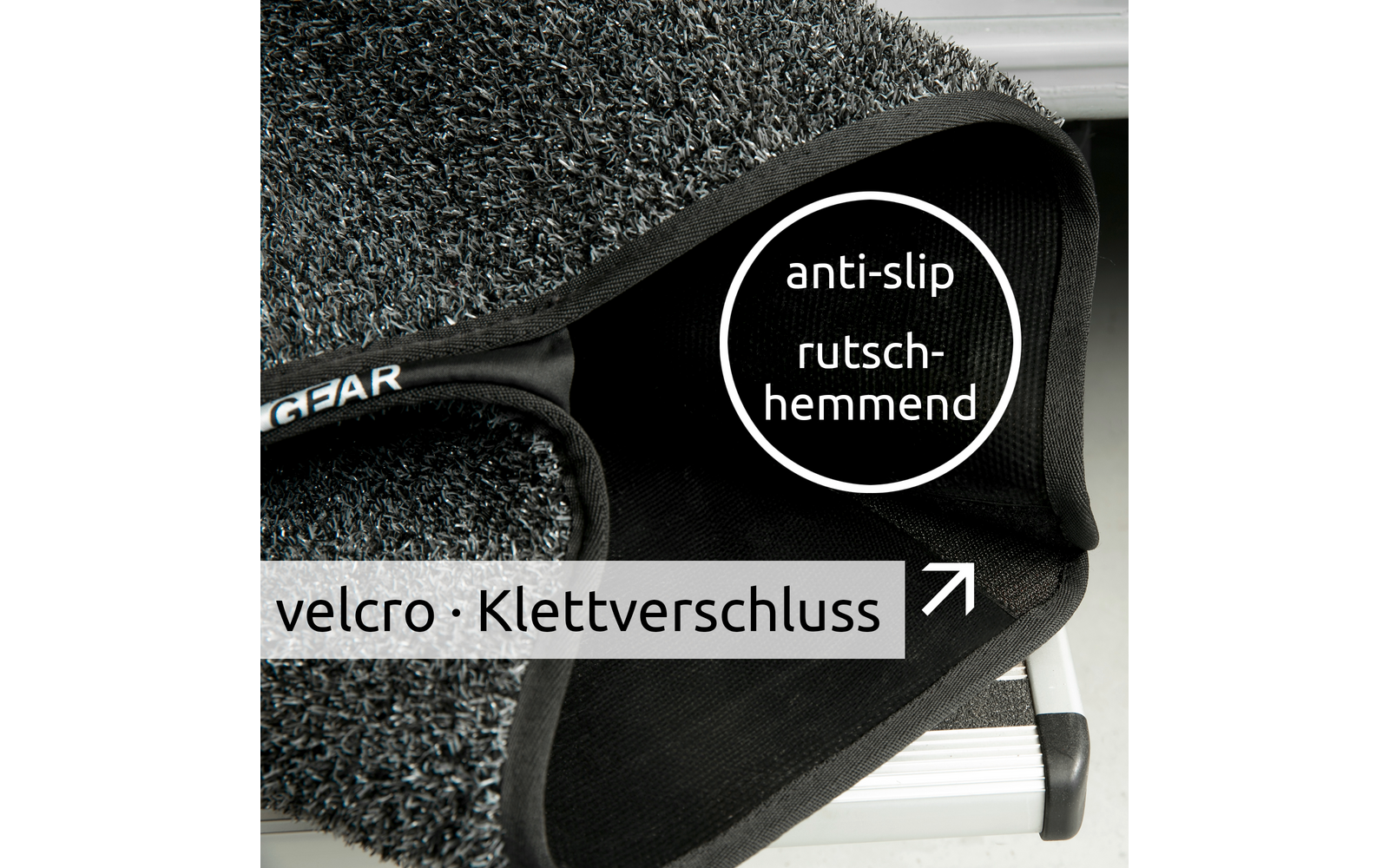 Nahaufnahme eines grauen, strukturierten Teppichstücks mit schwarzem Klettverschluss auf einer Metallstufe; sichtbare Texte 'anti-slip rutschhemmend' und 'velcro · Klettverschluss'